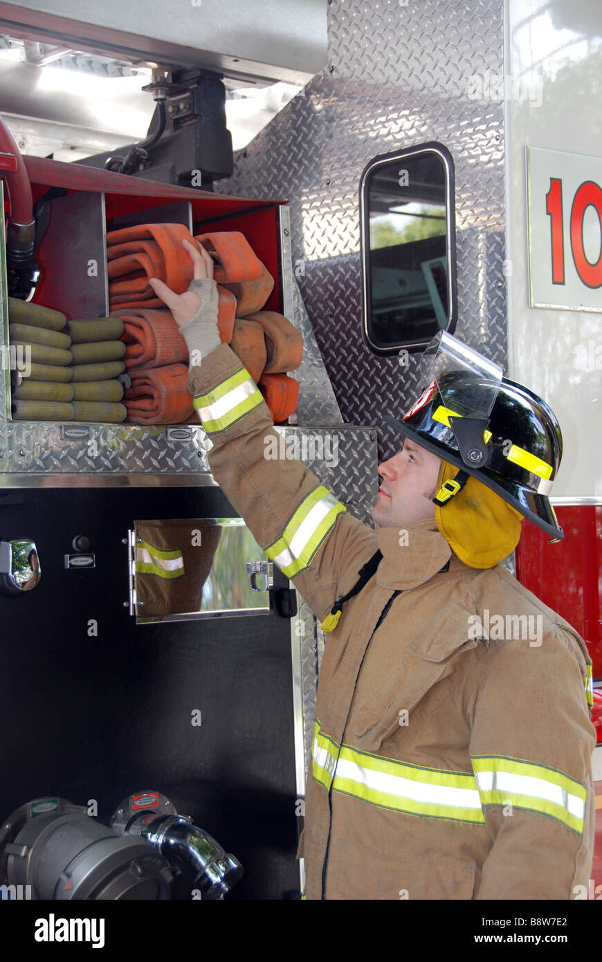 Male Firefighter reaching for fire hose on fire truck wearing bunker gear and helmet Stock Photo