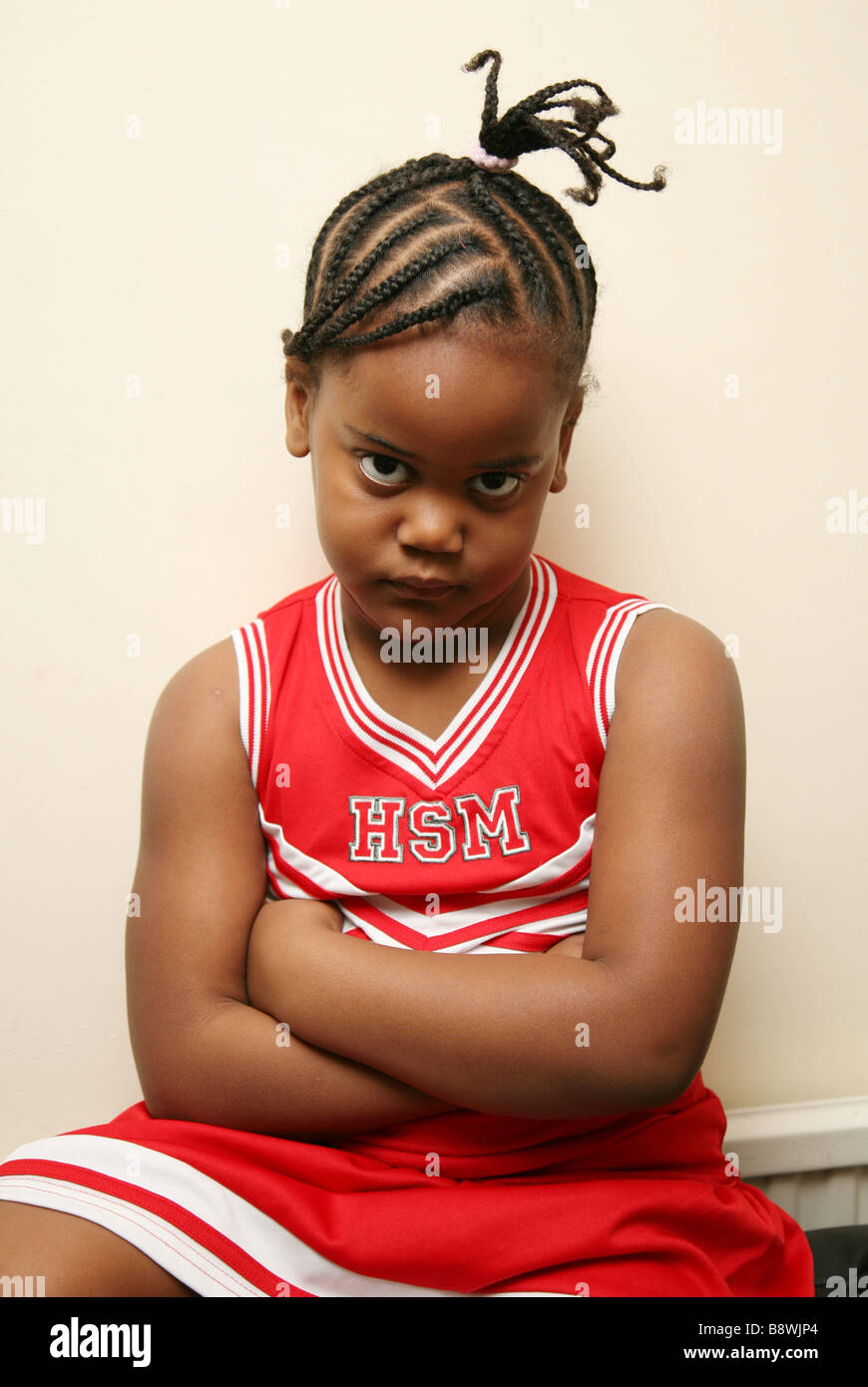 Sulking child sitting against the wall with her arms crossed Stock Photo