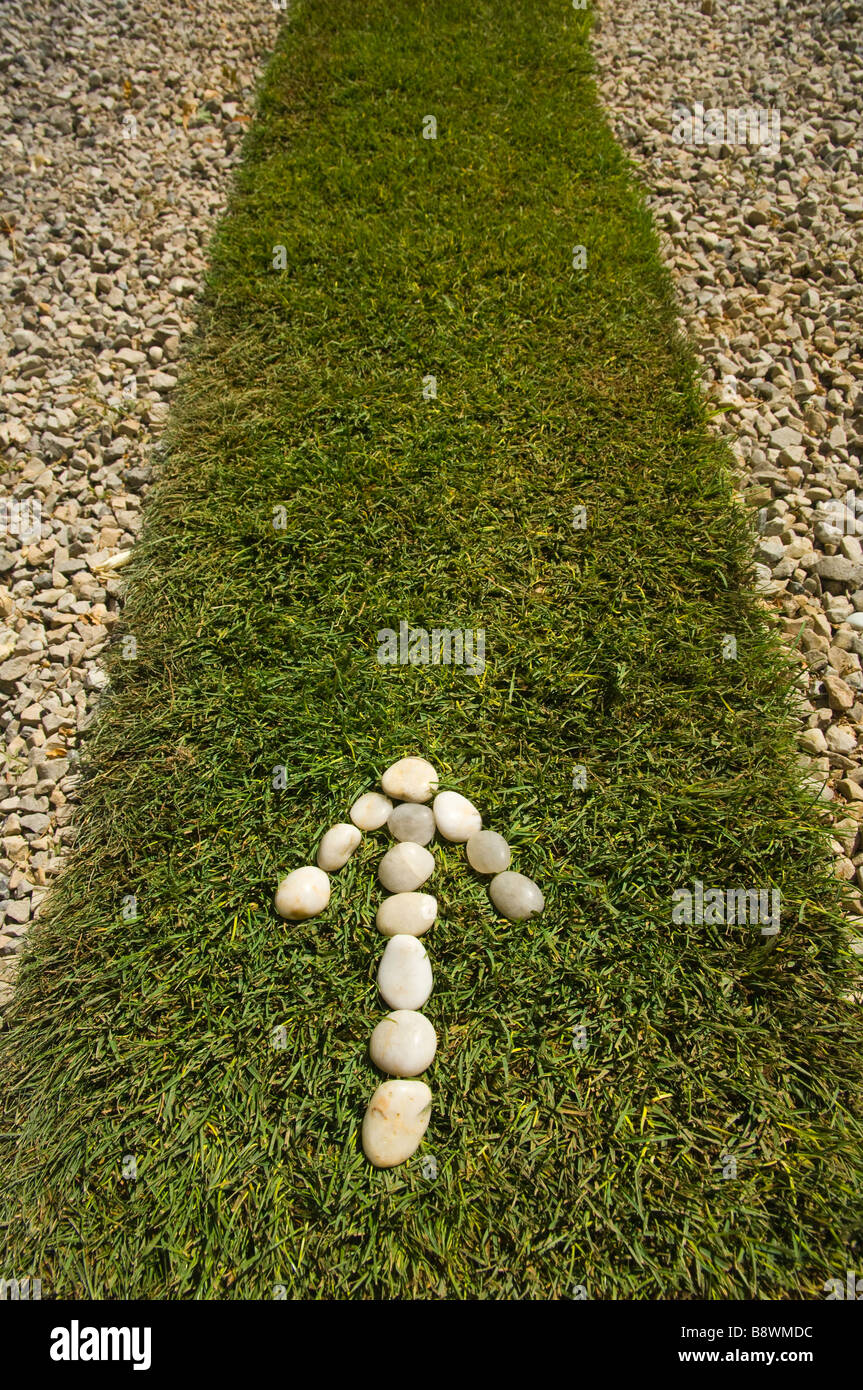 An arrow of white stones points a direction along a path of green grass over gravel, symbolizing environmental awareness. Stock Photo