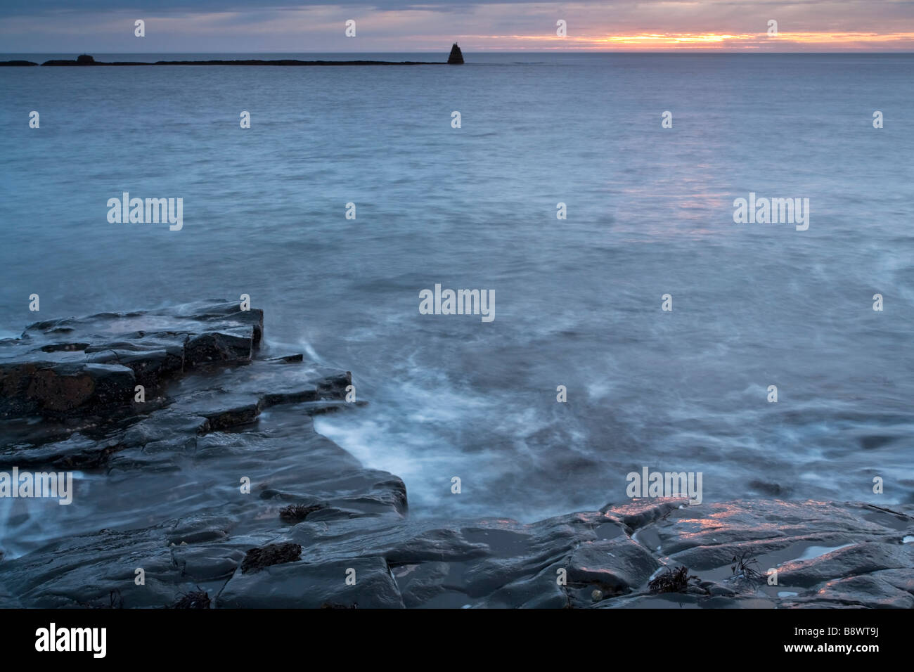 Black Whin Sill rocks on the Northumbrian coast bathed in the pink light of sunrise Stock Photo