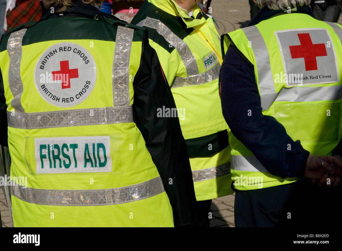 rear view of three First aid volunteer British Red Cross workers wearing high visibility yellow jackets, UK Stock Photo