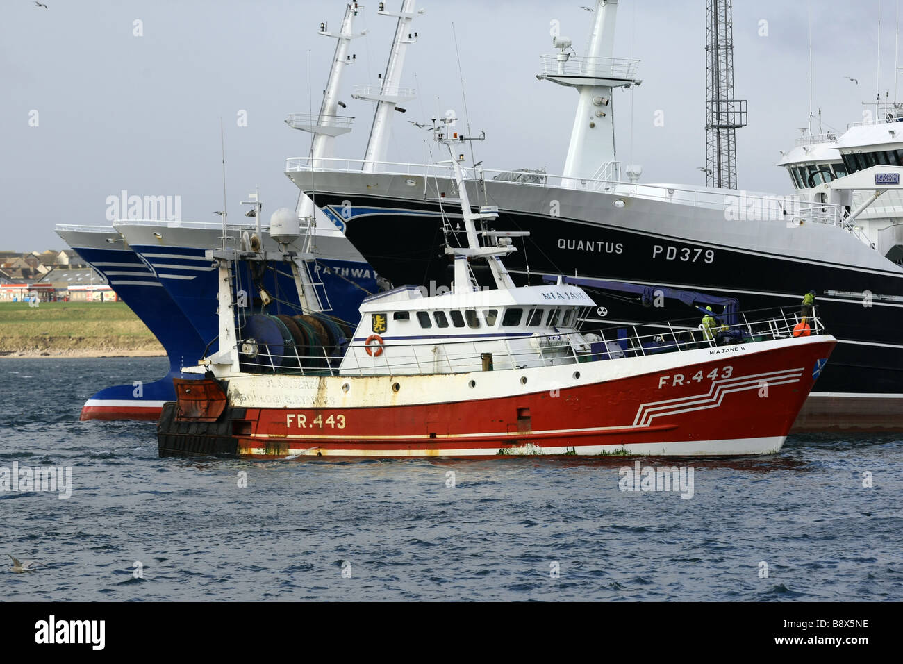 Red fishing trawler enters the harbour at Peterhead, Scotland, UK, passing much larger fishing vessels Stock Photo