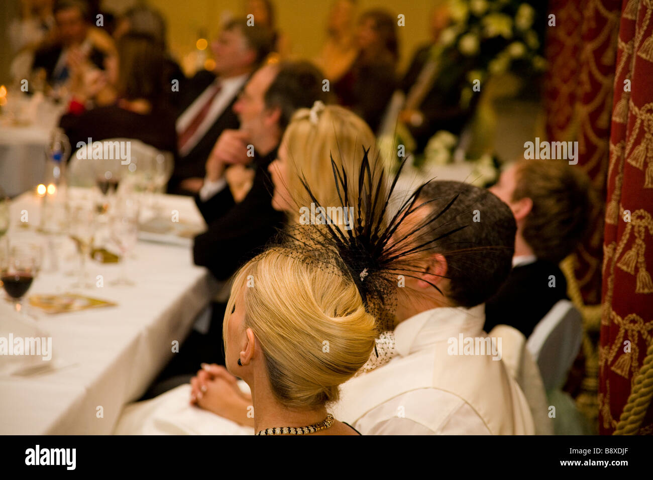 Elegant woman wearing a modern fascinator hat during speeches at a wedding reception. Stock Photo