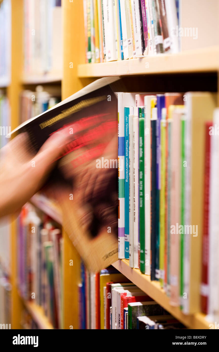 Hand taking out a book from a bookshelf in a library. Stock Photo