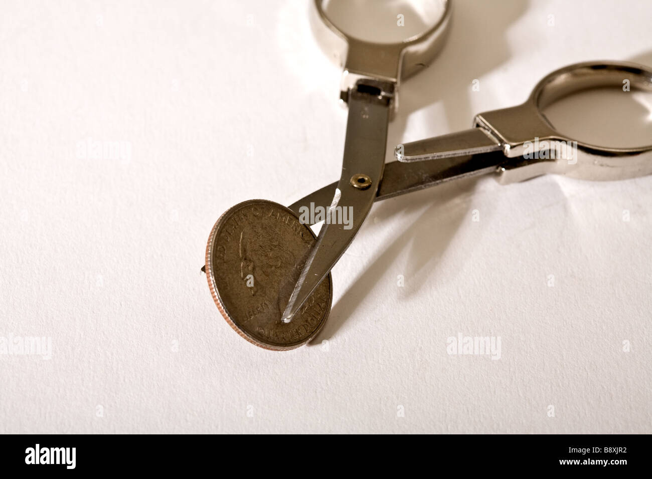 Small scissors cutting into a American quarter coin Stock Photo