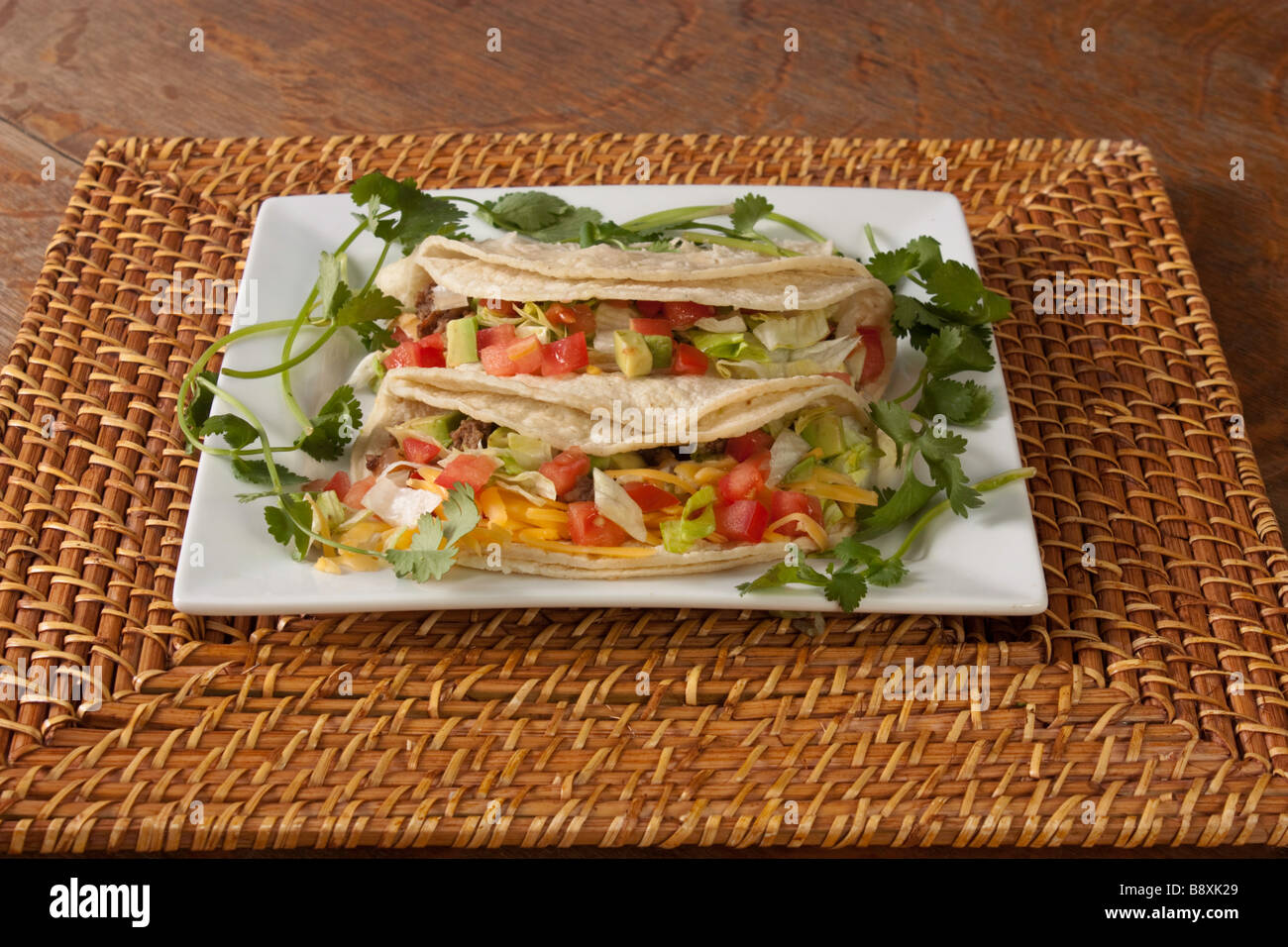 A plate of traditional style soft tacos on a bamboo charger garnished with cilantro Stock Photo