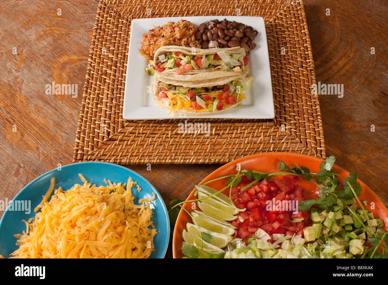 A plate of tacos rice and beans on a bamboo charger with taco ingredients on separate platters Stock Photo