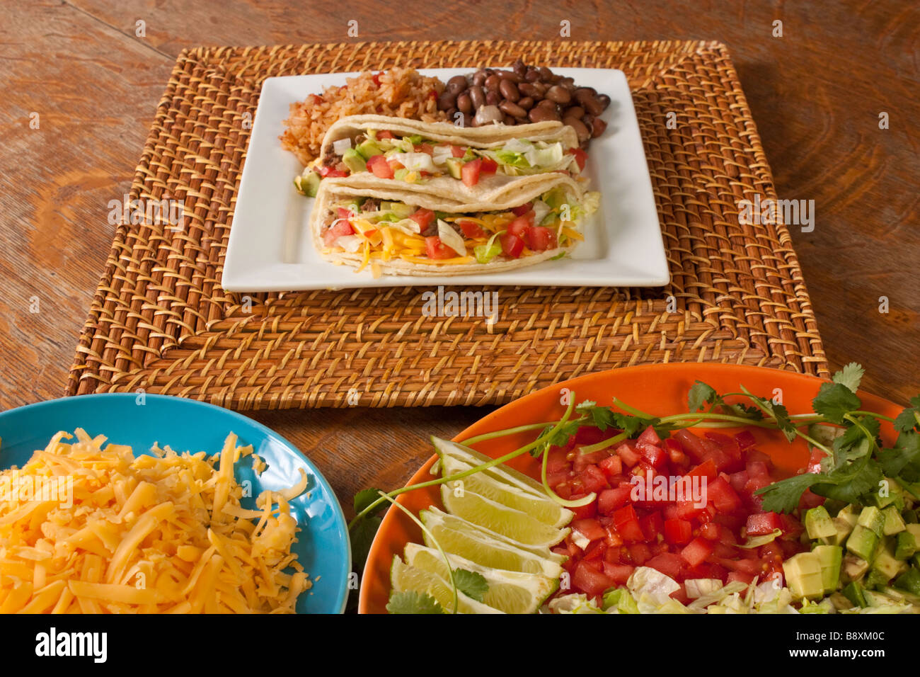 A plate of tacos rice and beans on a bamboo charger with taco ingredients on separate platters Stock Photo