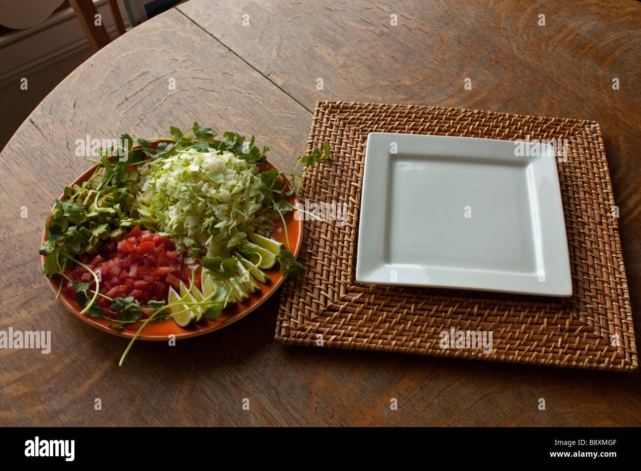 An empty plate on a bamboo charger and a platter of taco ingredients on an old wooden table Stock Photo