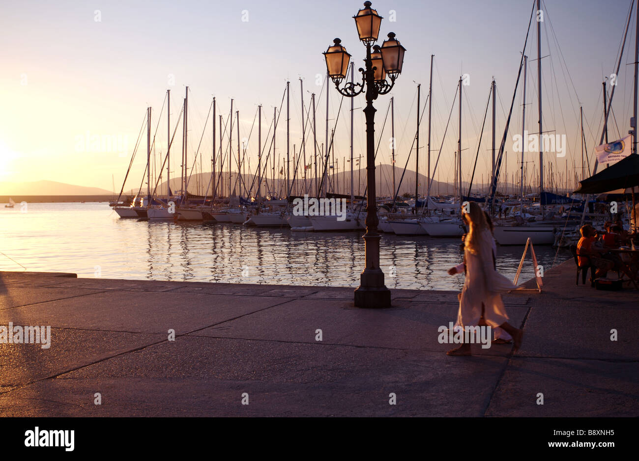two people walk along the promenade during sunset in alghero dressed in white Stock Photo
