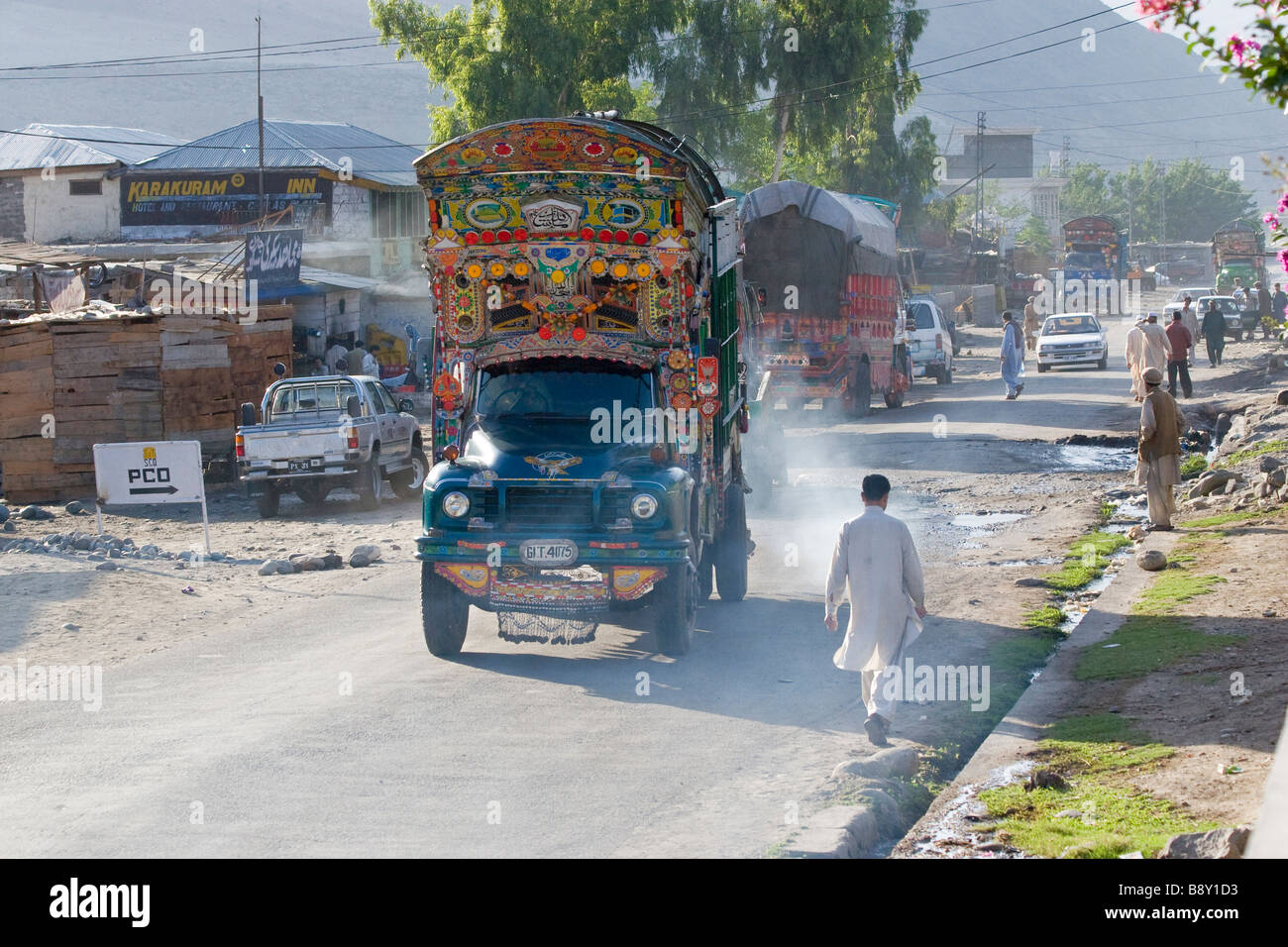 Ornate trucks cars and pedestrians on the main street of a town, Karakoram Highway, Pakistan Stock Photo