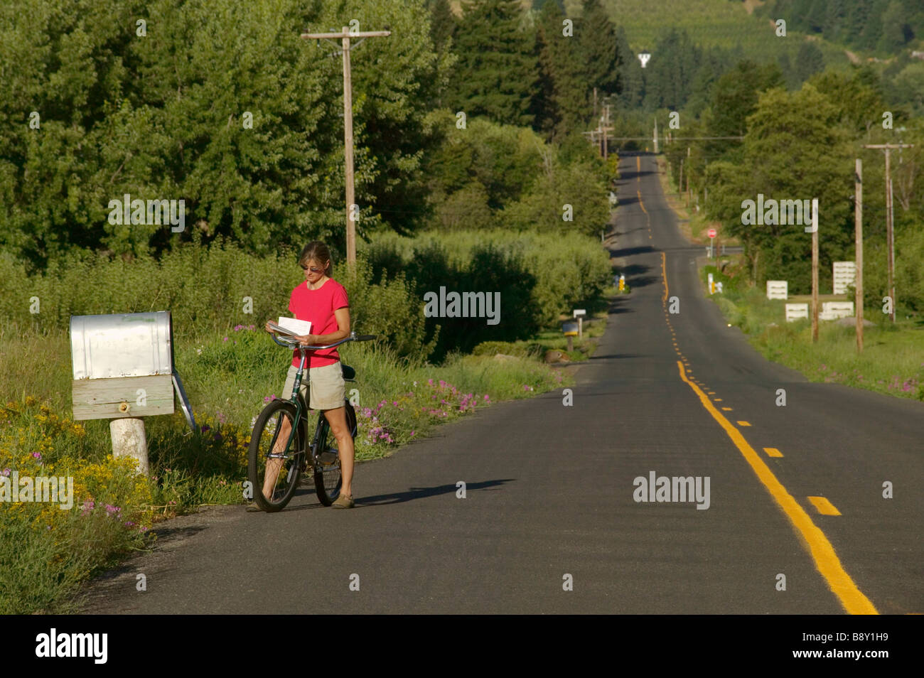 Woman reading a mail by a country mailbox while riding a bicycle, Parkdale, Hood River County, Oregon, USA Stock Photo