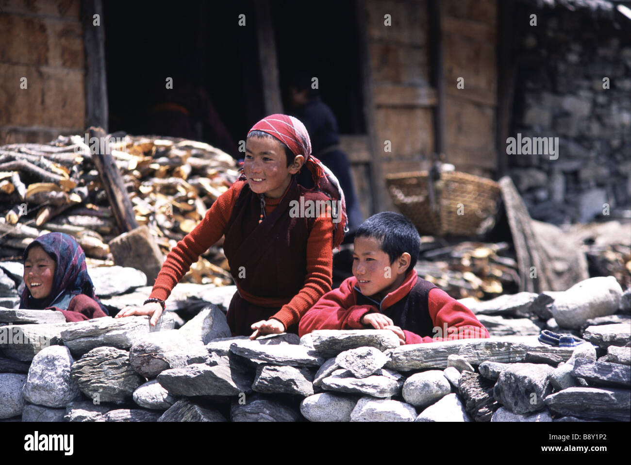 Two girls and a boy standing behind a stone wall, Samagaon Village, Nepal Stock Photo