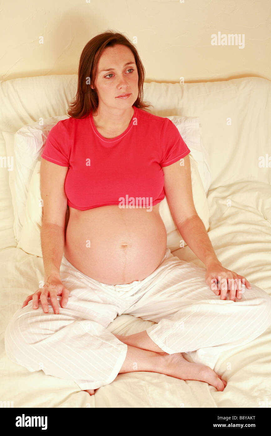 Heavily pregnant young woman sitting relaxing cross legged at home 32 weeks third trimester glowing happy contented healthy Stock Photo