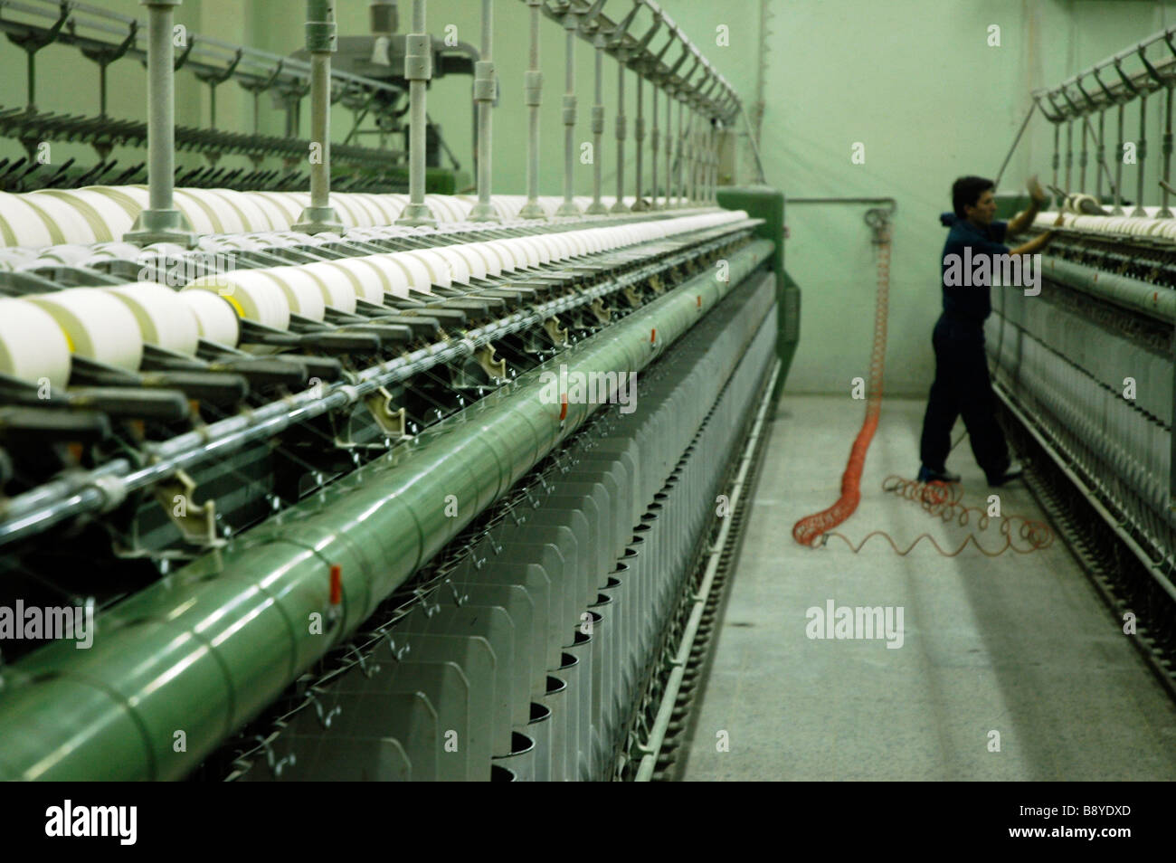 man working in cotton processing factory, he stands at the end of a line of machines Stock Photo