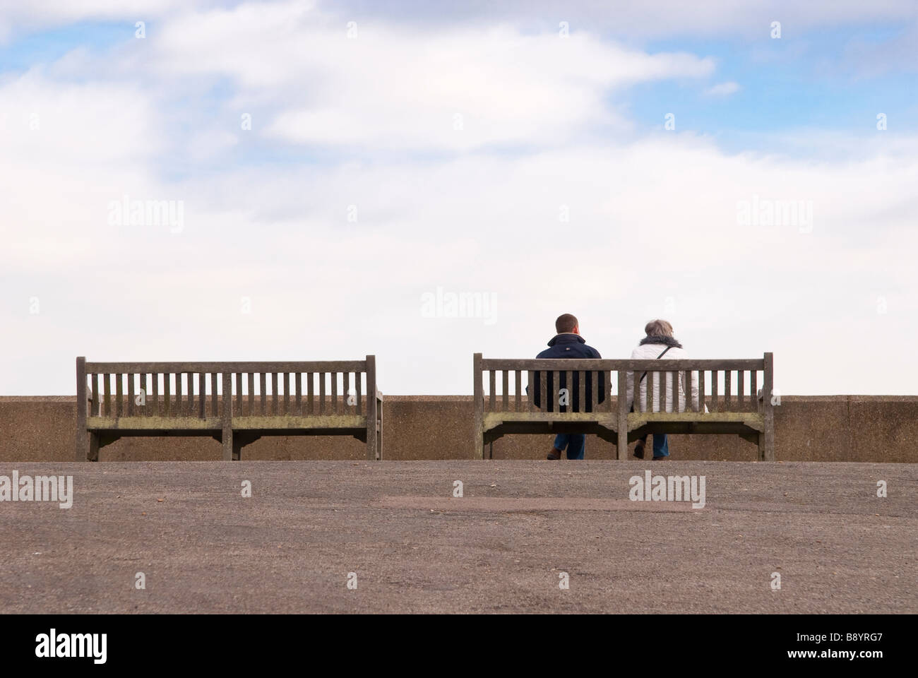 An isolated couple sitting on a coastal bench near the sea wall looking ...