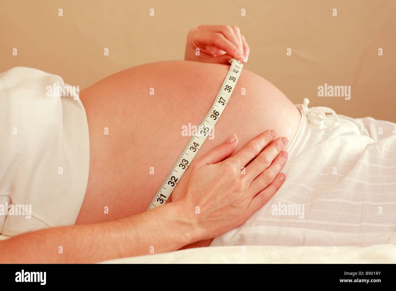 Closeup of healthy heavily pregnant woman measuring her growing bump stomach unborn child baby foetus with tape measure Stock Photo