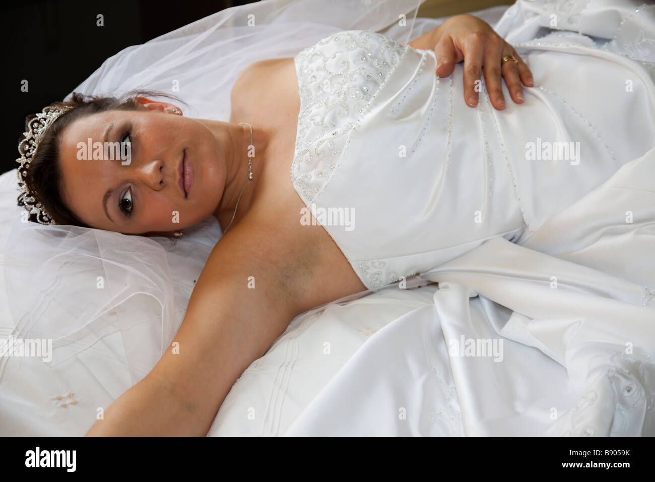 Bride laying on floor side view pose, in white embossed wedding gown with veil and tiara Stock Photo