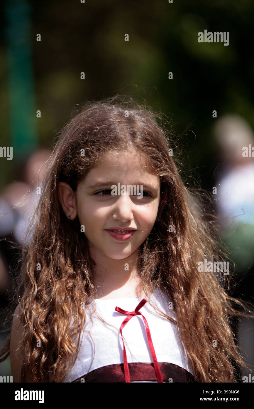 A young girl with long brown hair smiles whilst looking away in sunshine Stock Photo