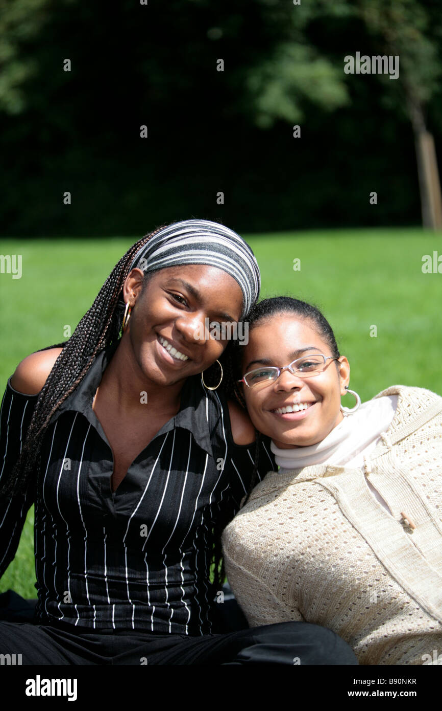 Two black girls smile whilst sitting enjoying the sunshine in a park Stock Photo