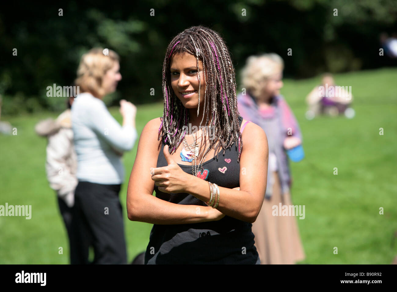 A attractive girl with pink braided hair in dreadlocks in a black vest gives the thumbs up in a park Stock Photo