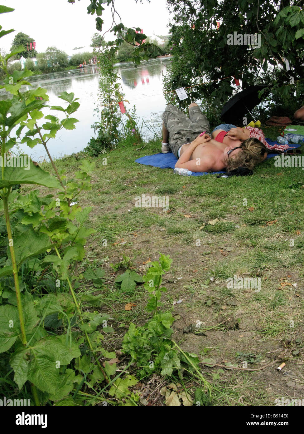 Two festivalgoers sleeping by a lake during The Secret Garden Party 2008, UK Stock Photo