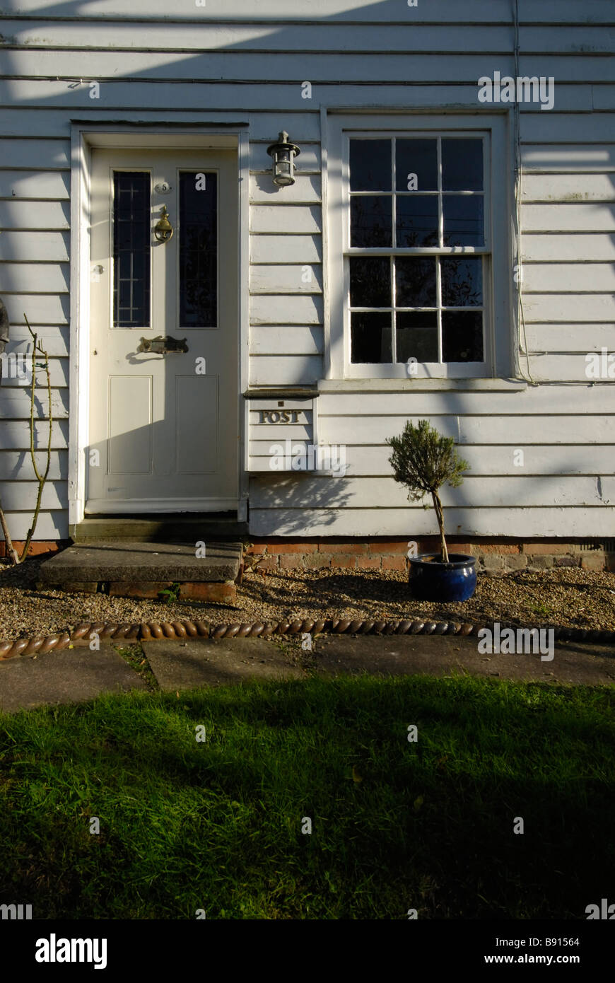 old white clapboard house front with door & window long shadows Stock Photo