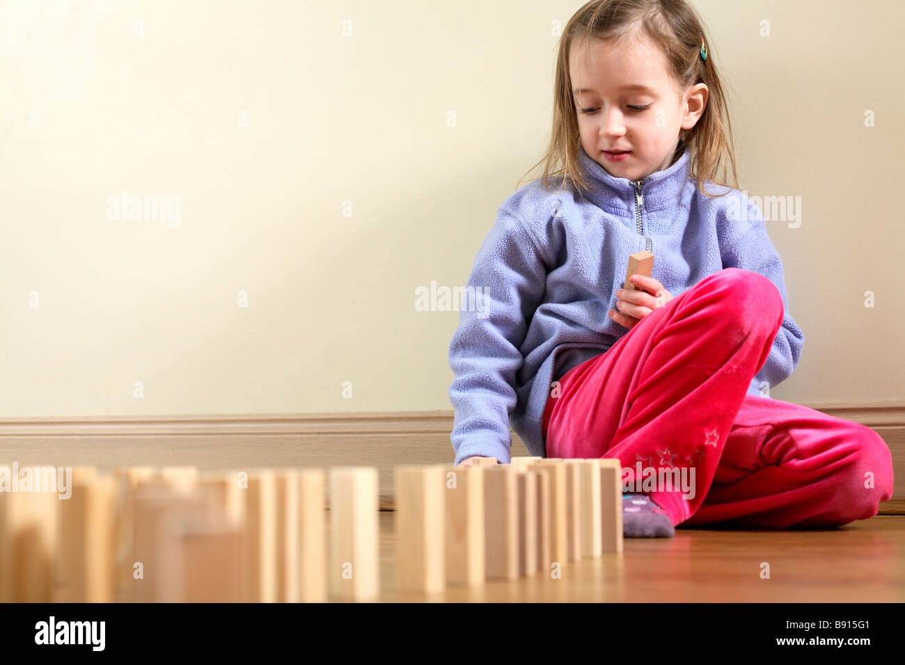Young girl setting up wooden building blocks to play domino tumbling Stock Photo