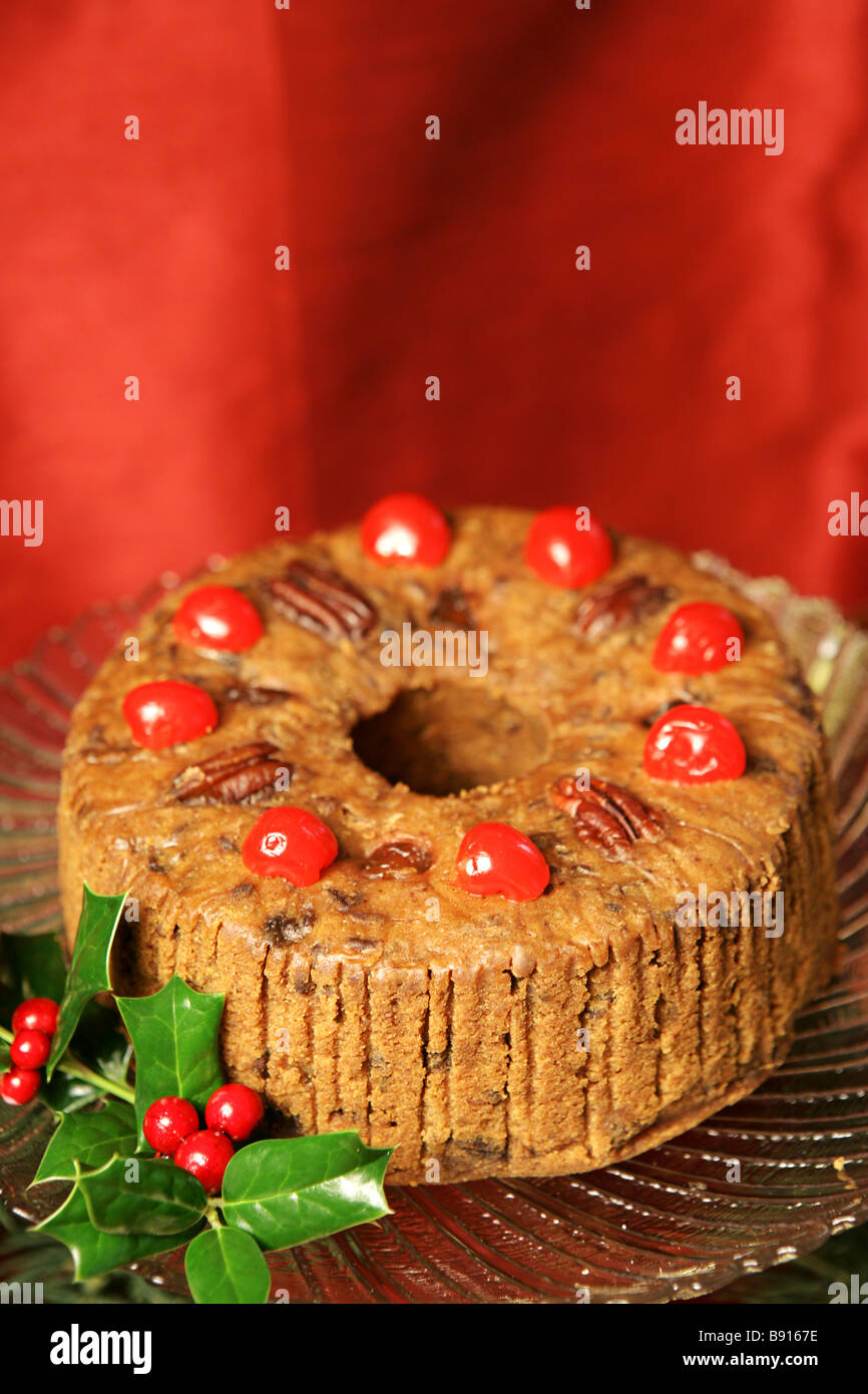 Beautiful Christmas fruitcake with holly garnish on a red draped silk background Vertical with room for text  Stock Photo
