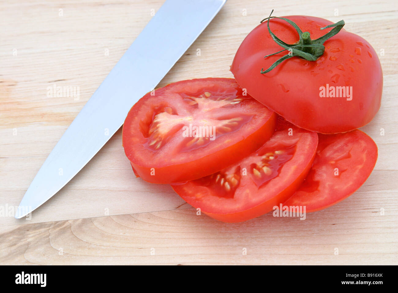 A sliced tomato and a knive on a wood cutting board Stock Photo - Alamy