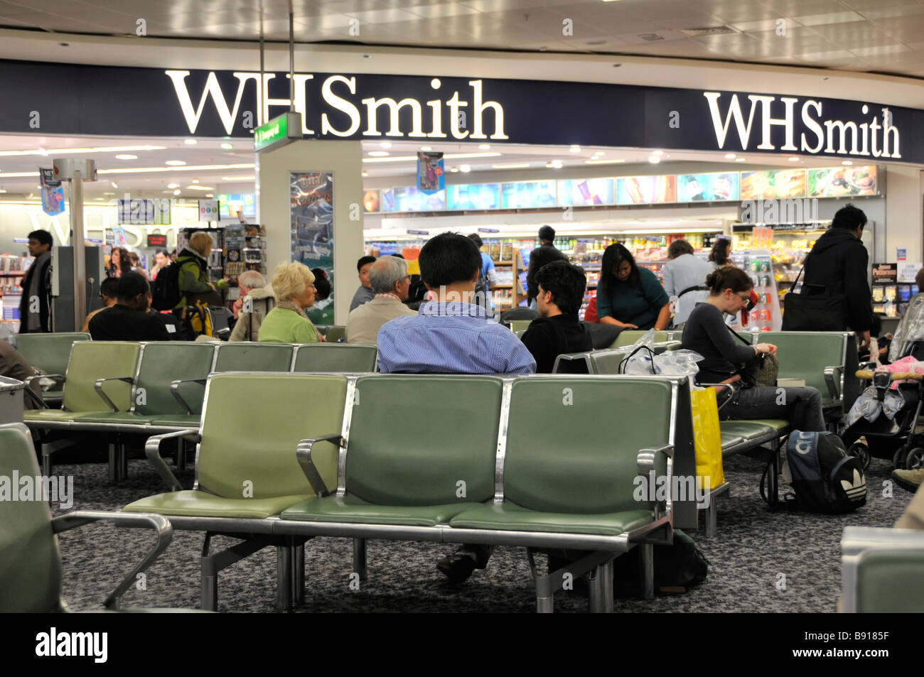 London Heathrow Airport terminal 3 interior passengers in departure lounge waiting for boarding instructions beside WH Smith newsagents England UK Stock Photo