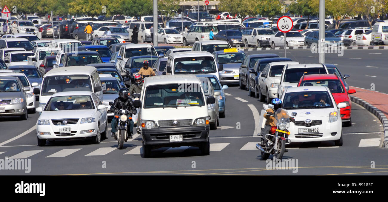 Dubai close up busy wide road junction cars & motorbikes in traffic moving off at lights surface car park beyond United Arab Emirates UAE Middle East Stock Photo