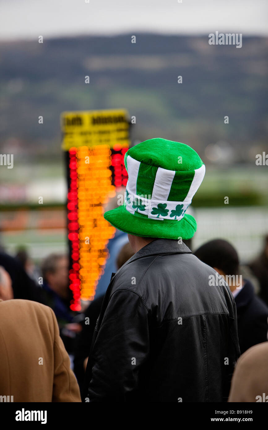 An Irish betting punter checks the odds on an electronic board while wearing a large green shamrock emblemed hat Stock Photo