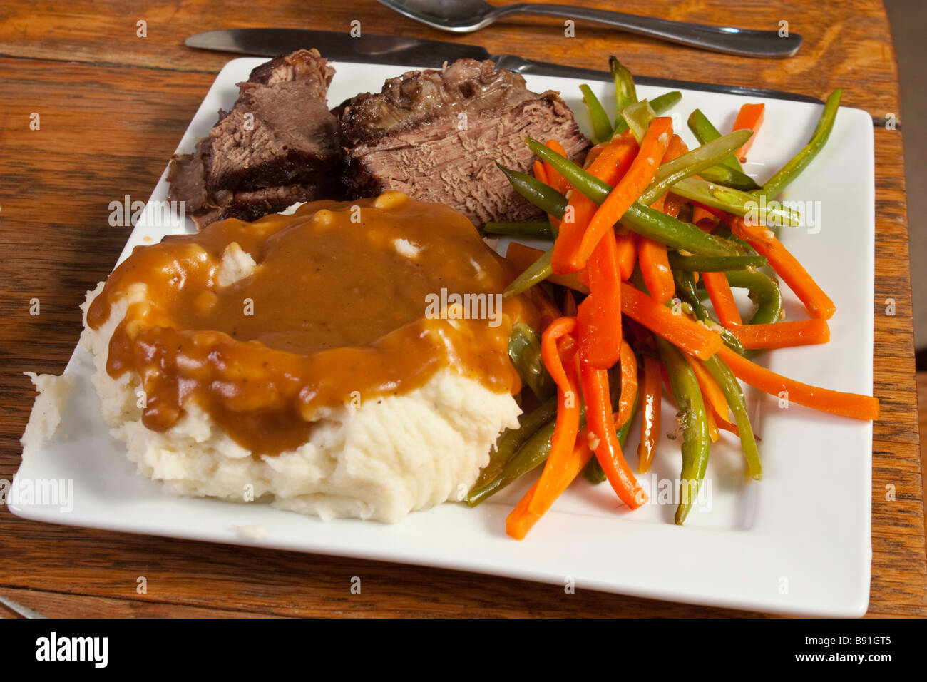 Mashed potatoes, gravy, pot roast with julienned green beans and carrots on a white plate Stock Photo