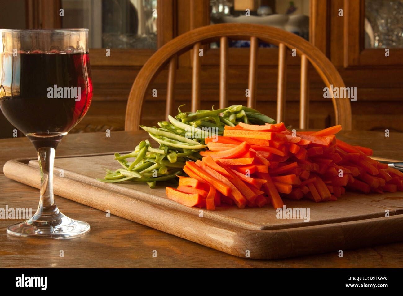 A cutting board with jullienned carrots and green beans with a knife and a glass of wine for the chef Stock Photo