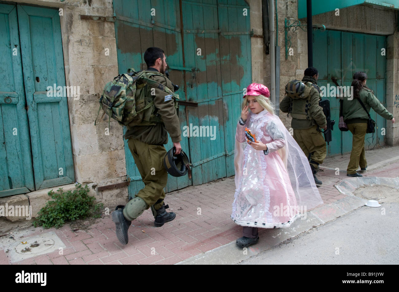 A young Jewish settler wearing a costume walks past Israeli soldier patrol during Purim feast in Al-Shuhada Street closed to Palestinians in Hebron Stock Photo