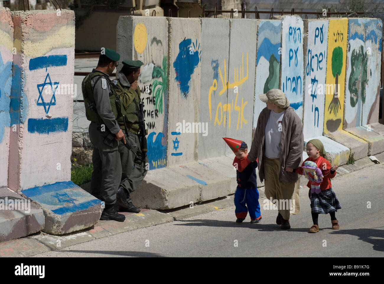 Jewish settlers walking along concrete slabs separating Palestinian neighborhood of Bab a-Zawiya and H-2 Israeli control area in Hebron West Bank Stock Photo