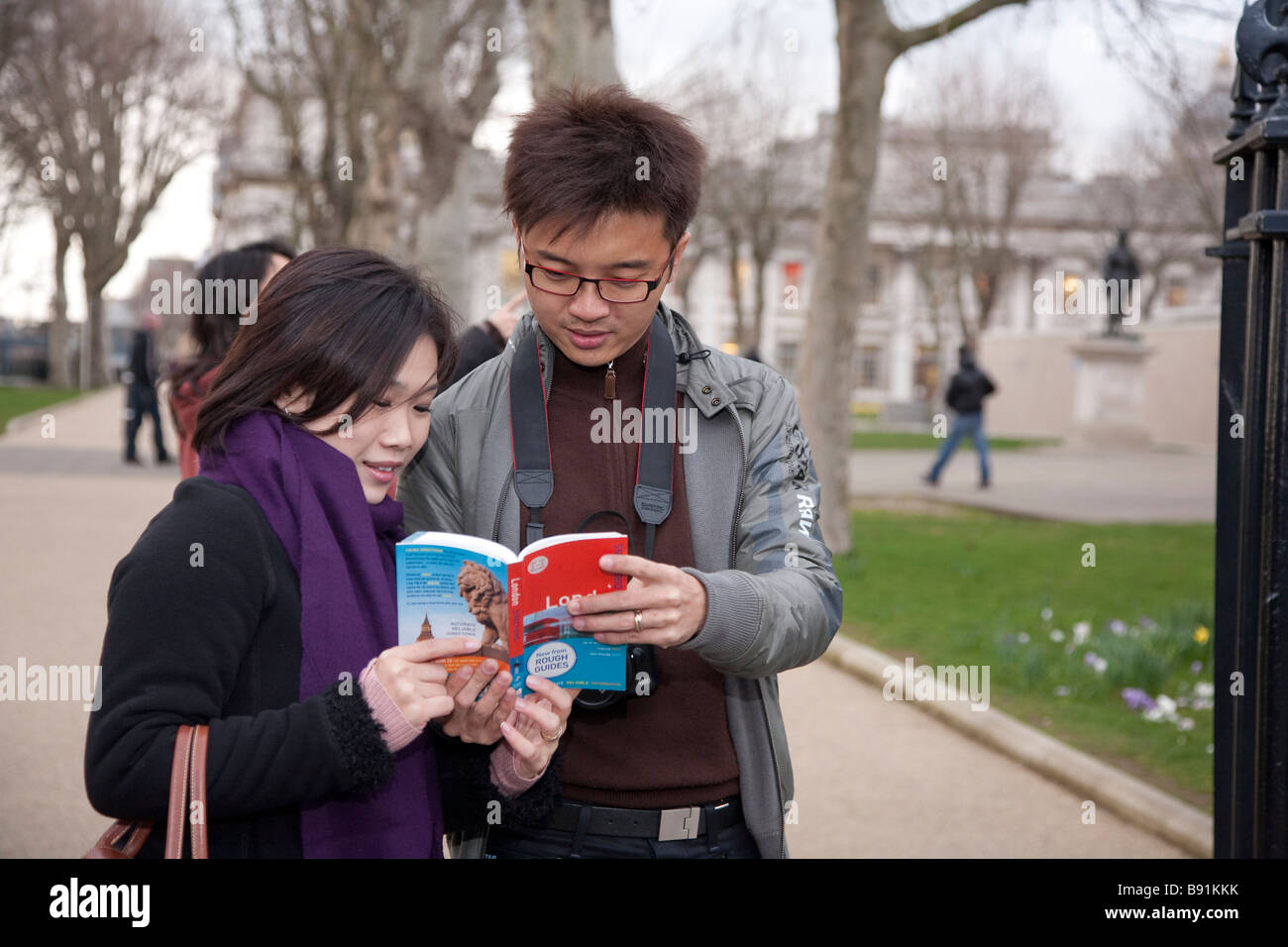 Asian oriental tourist couple in 20s / 30s visiting London, consulting a guide book outside the Royal Naval College Greenwich Stock Photo