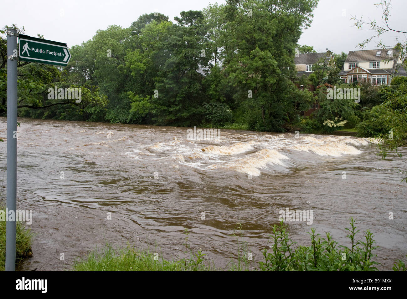 Footpath sign points to public footpath route across River Wharfe  (stepping stones submerged by fast flowing water) - Ilkley, Yorkshire, England, UK. Stock Photo