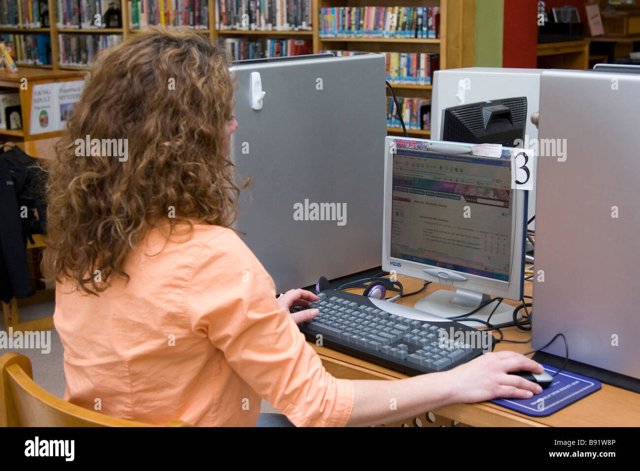 A young woman uses a computer at a public library to do research on the internet. Stock Photo