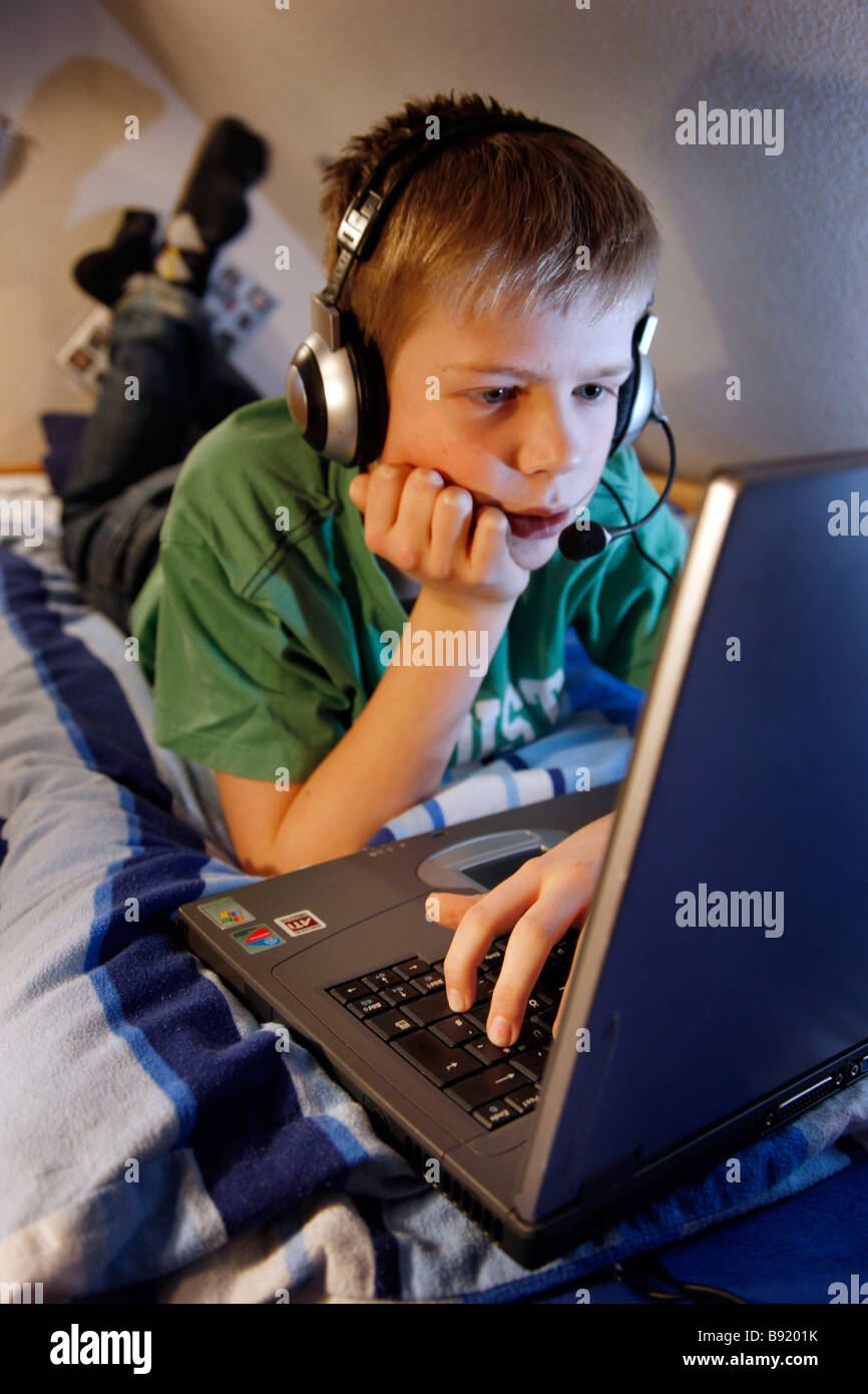 A boy, 13 years old, is chatting in his child room and talks to a chat member by voice over ip. He wears a headset. Stock Photo