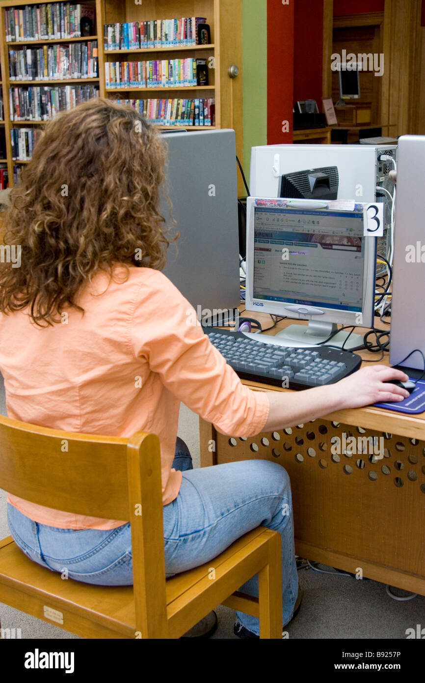 A young woman uses a computer at a public library to do research on the internet. Stock Photo