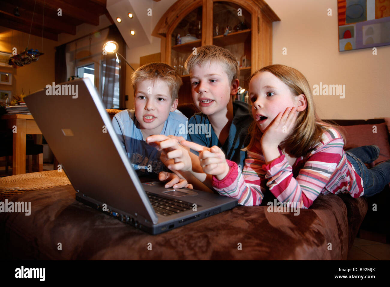 2 brothers and her sister, 7, 11 and 13 years old, playing a learning game, a quiz, at home. Stock Photo