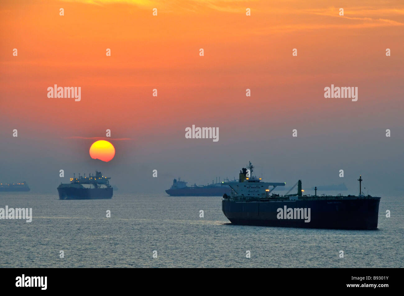 Sunset haze & shipping including unladen bulk carriers & oil tankers coastal anchorage UAE Fujairah bunkering port Gulf of Oman near Straits of Hormuz Stock Photo