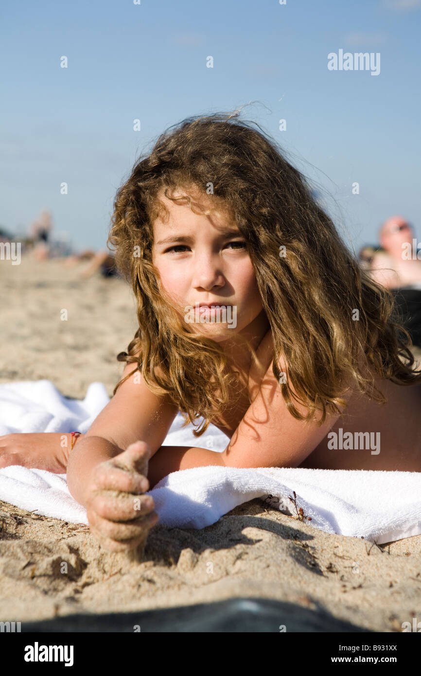 Child with sad expression lying on the sand. Stock Photo