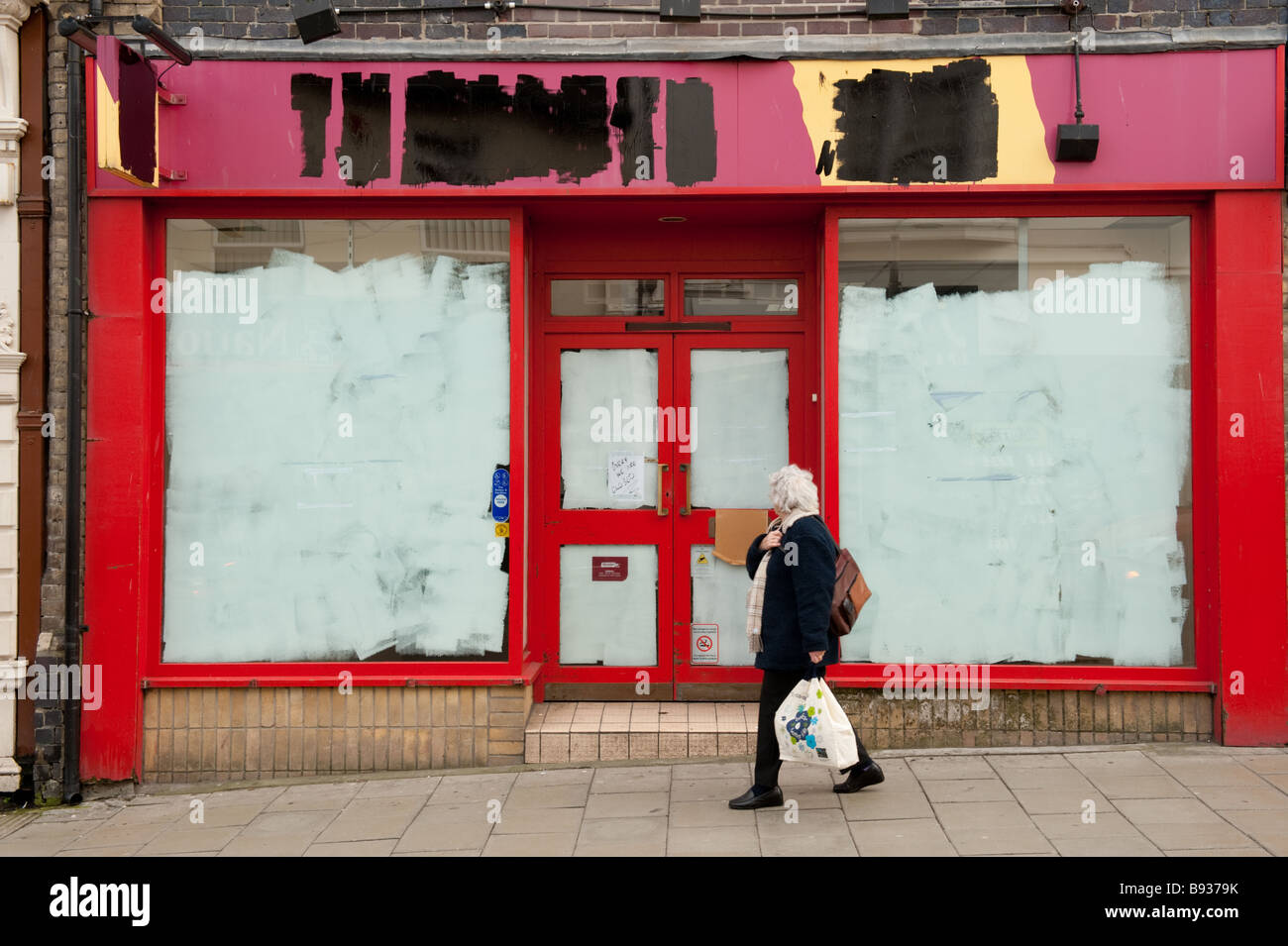 A woman walking past a closed shop (Threshers wine off licence) with painted out windows and shop name UK Stock Photo