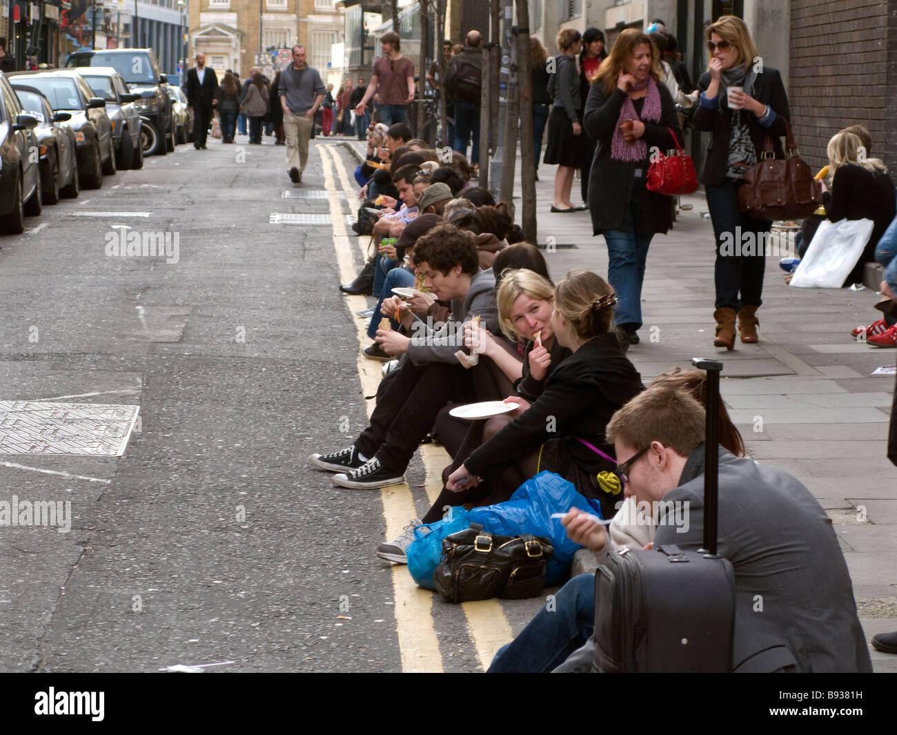 Youths sitting on kerb side eating take away food. Stock Photo