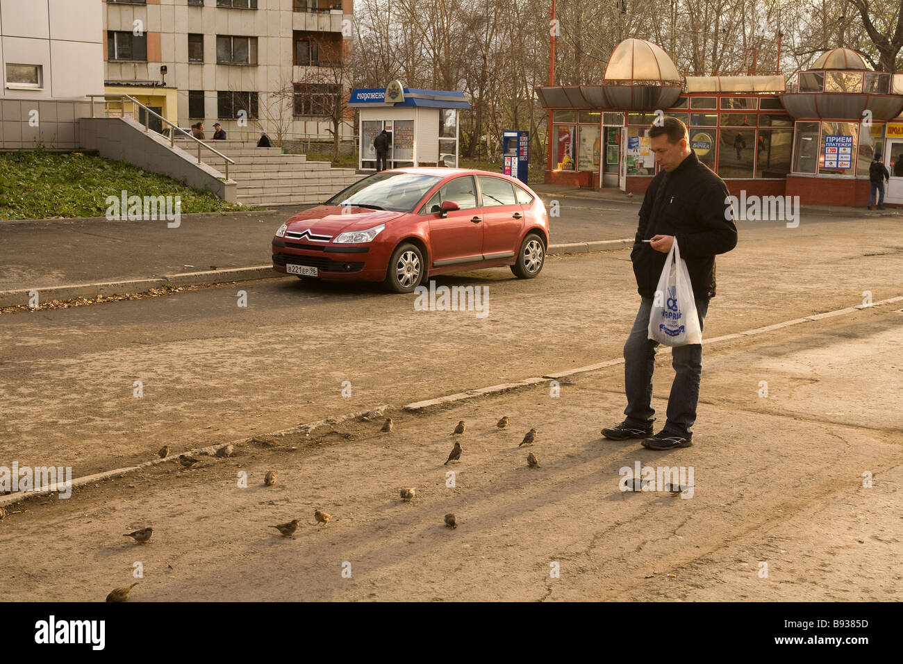 Man feeding birds outside apartment block, Ekaterinburg, Russia Stock Photo