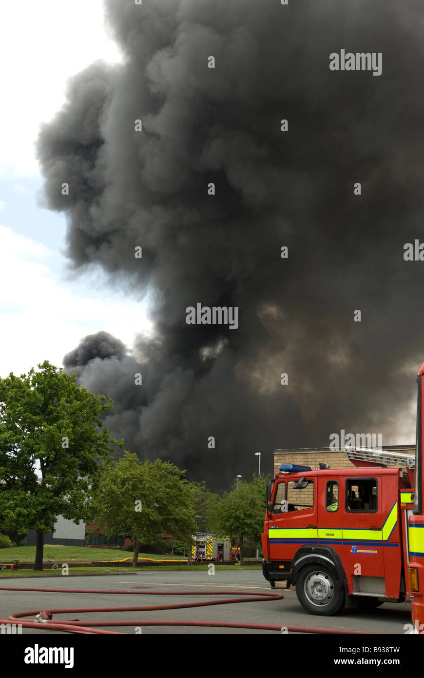 Fire Engine near large black cloud of smoke at factory fire . Portrait Format Stock Photo
