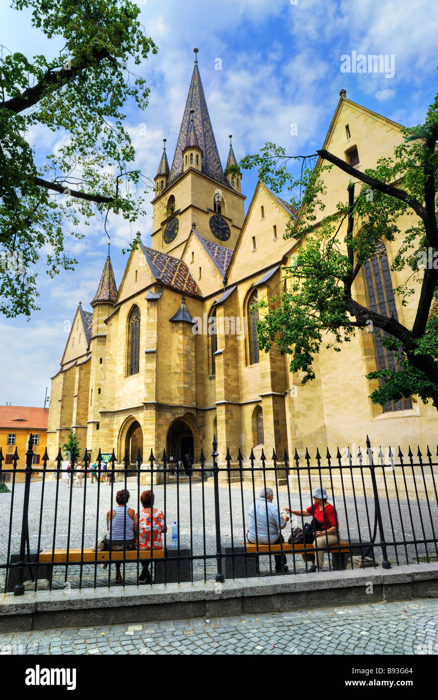 Tourists sitting on park benches outside the Biserica Evanghelica Sibiu Romania Stock Photo